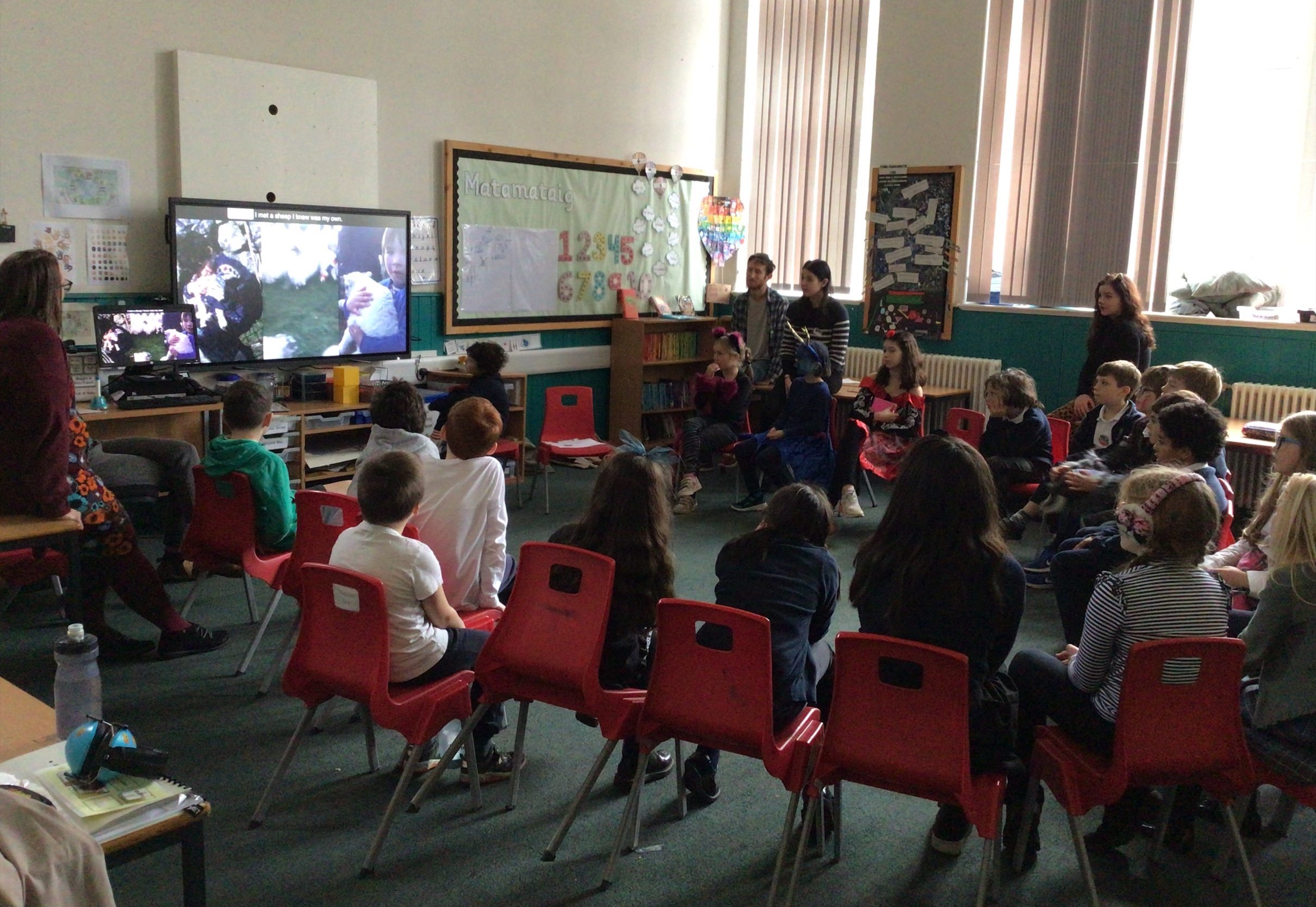 A group of children watching a film on a monitor in a classroom. Amaya is sitting to the left of the monitor.